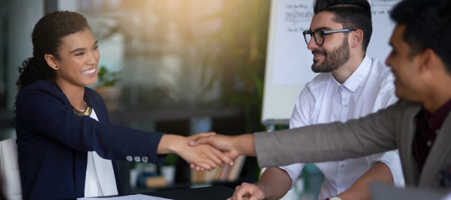 man shaking woman hand with another man at a table in a business meeting